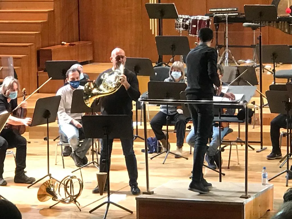 Oscar Sala tocando la trompa de pie, delante de la orquesta, durante un ensayo